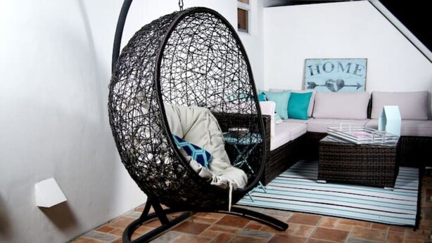 Un salon chaleureux avec un fauteuil suspendu, un canapé et un panneau décoratif représentant le mot « MAISON » accroché au mur.