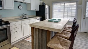 Una cocina con armarios blancos, un refrigerador de acero inoxidable, un reloj y una ventana con persianas.
