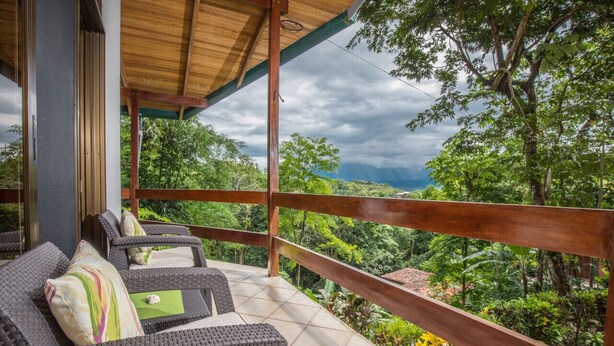 Un espacio de estar techado al aire libre con mobiliario de mimbre y vistas a abundante vegetación.