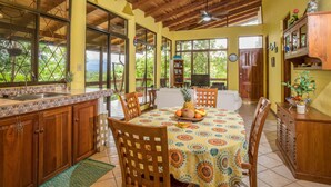 Una cocina amplia con armarios de madera, una mesa de comedor con sillas y un ventanal con vistas a la vegetación.