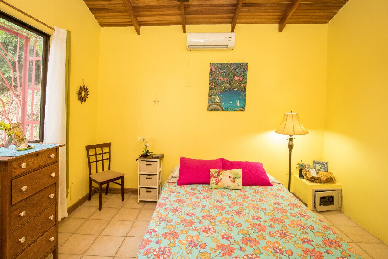 A room with a bed, a dresser, a chair, a nightstand, a lamp, and a painting on the wall.