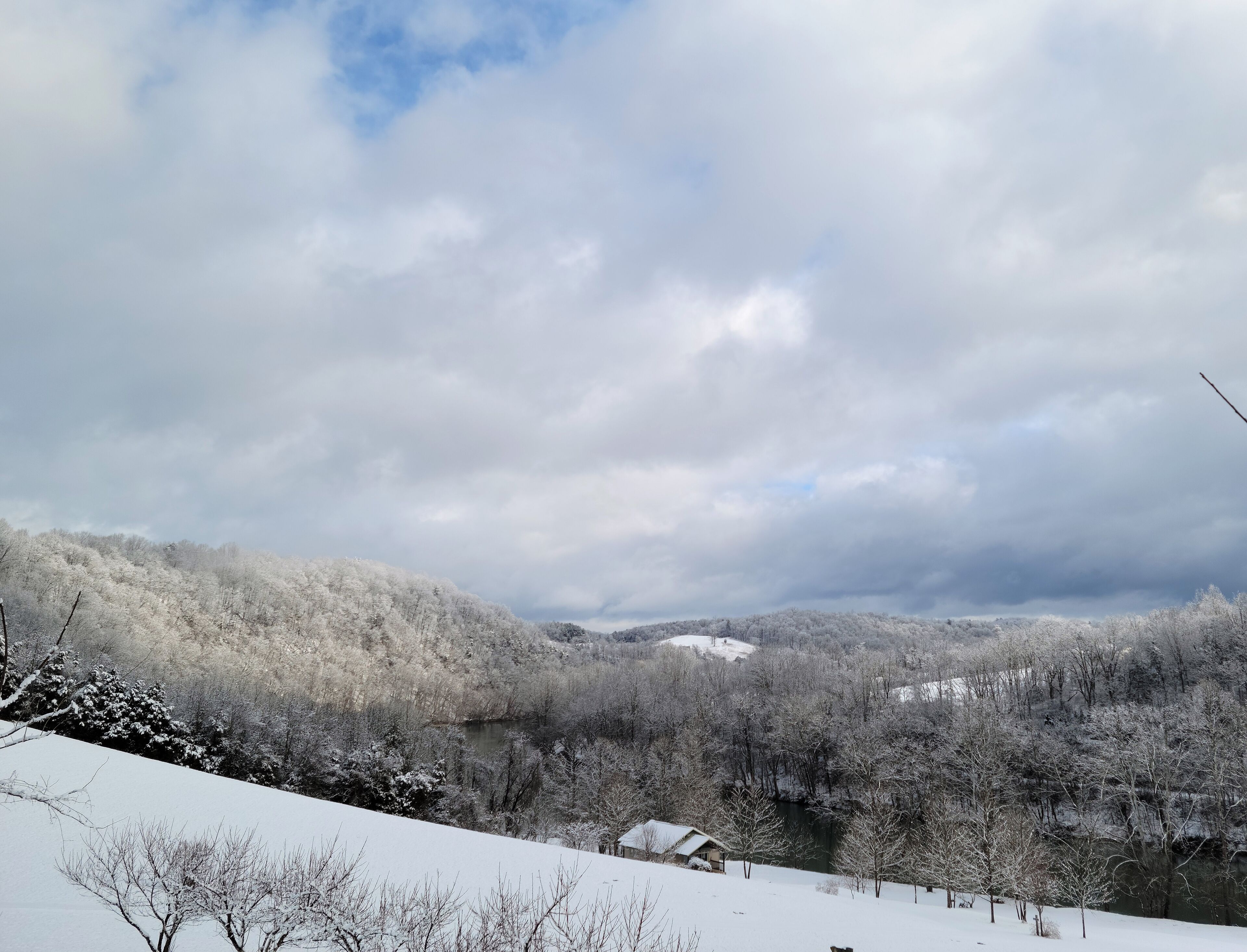 Schneebedeckte Landschaft mit Fluss, Bäumen und einem kleinen Gebäude.