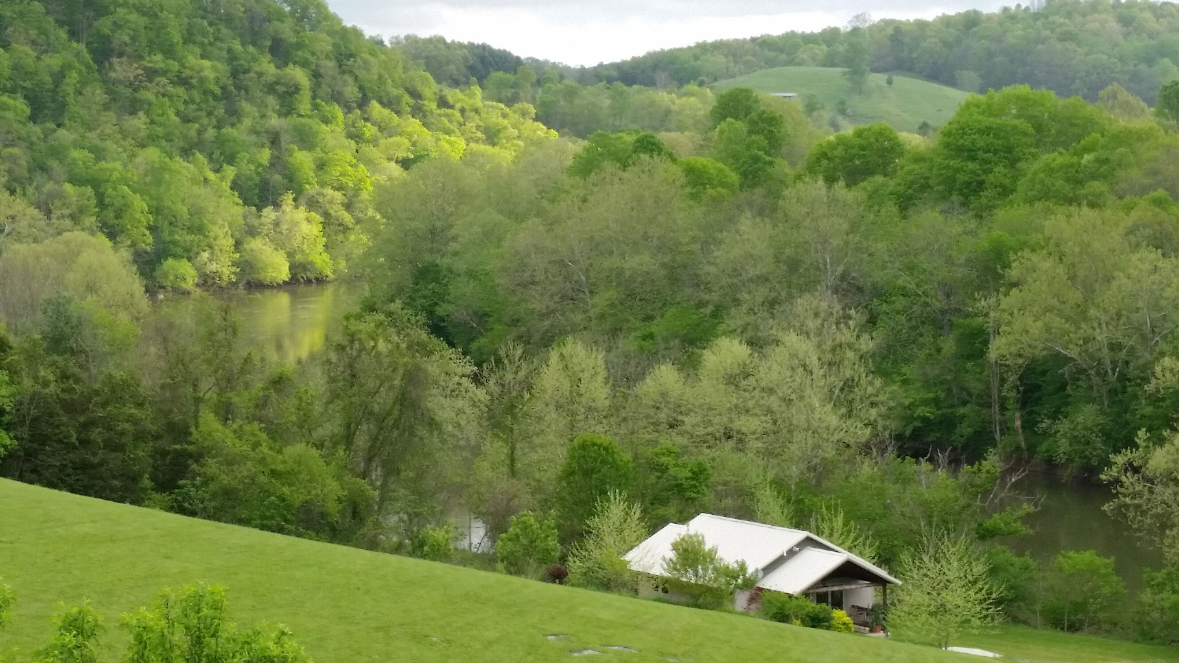 A rural landscape with a house on a hill overlooking a river.