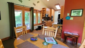 Un'accogliente sala da pranzo con tavolo e sedie in legno, una cucina con pensili in legno e vista sul giardino attraverso le finestre.