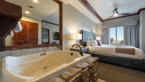 Une chambre d’hôtel avec une grande baignoire, un lit avec une tête de lit, une table de chevet, une lampe et une vue sur l’extérieur.