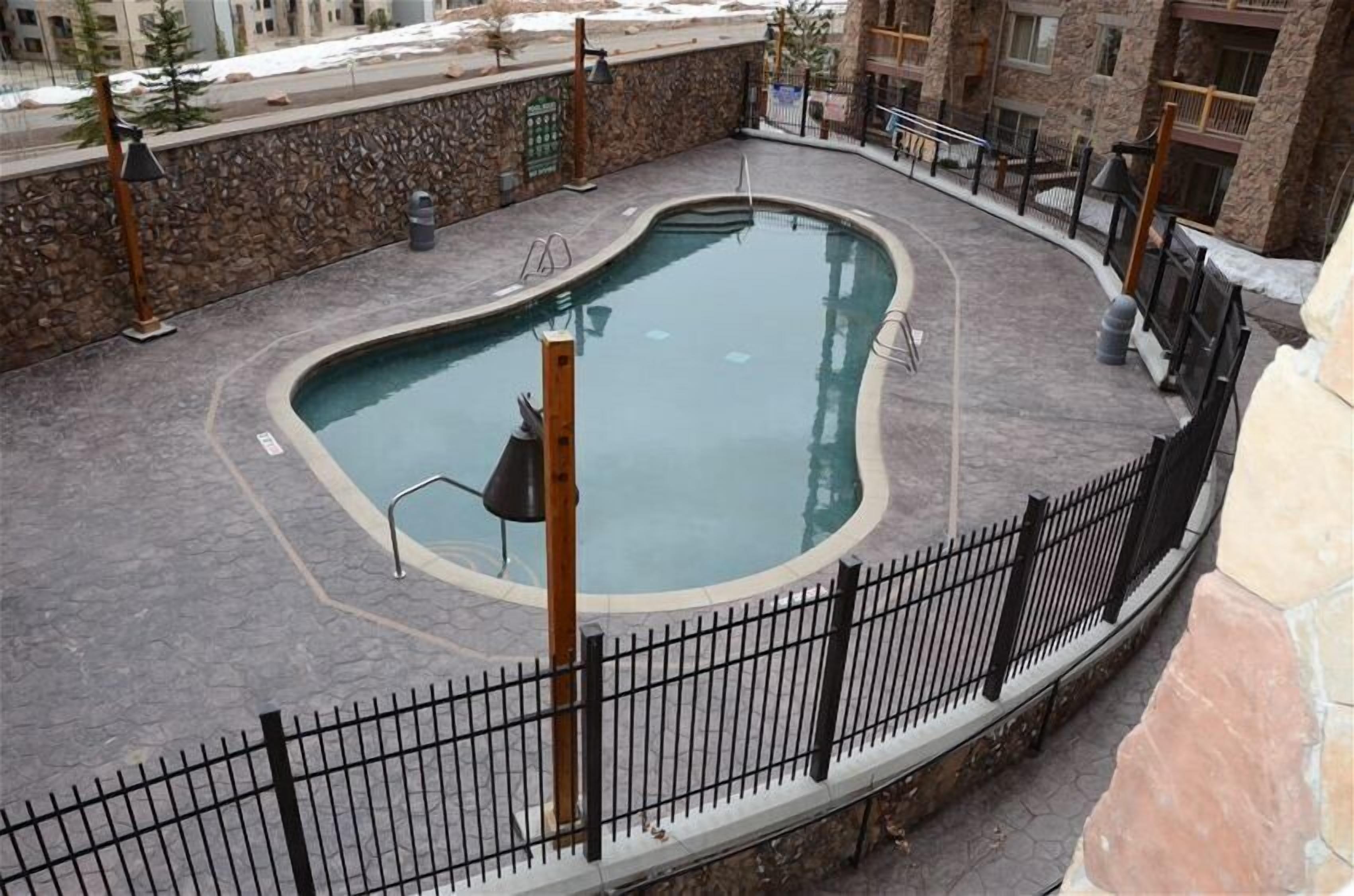 A swimming pool with a curved edge, surrounded by a stone wall and a black metal fence.