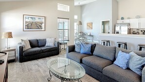 En moderne stue med sofalounge, spiseplads og et glasbord. Loftvifte er også inkluderet.