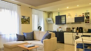 Ein modernes Wohnzimmer mit einem beigen Sofa, einem Couchtisch und einem Essbereich mit einem weißen Tisch und blauen Stühlen.