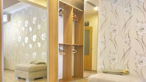 Ein Zimmer mit einem raumhohen Spiegelkleiderschrank, einer gepolsterten Sitzbank und einem floralen Wandbehang.