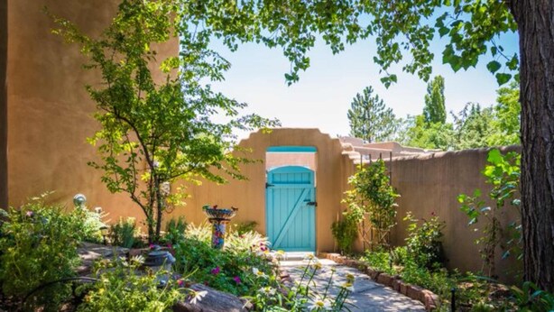 A garden with a blue gate, surrounded by various plants and a decorative bird bath.