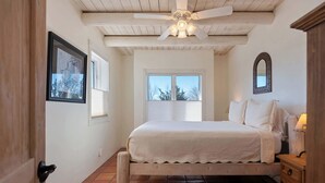 A bedroom with a bed, a wooden headboard, a nightstand, a mirror, and a ceiling fan.