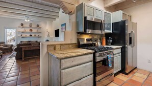 A kitchen with a stove, oven, microwave, and refrigerator. There is a dining area with a table and chairs. The kitchen has wooden cabinets and a tiled floor.