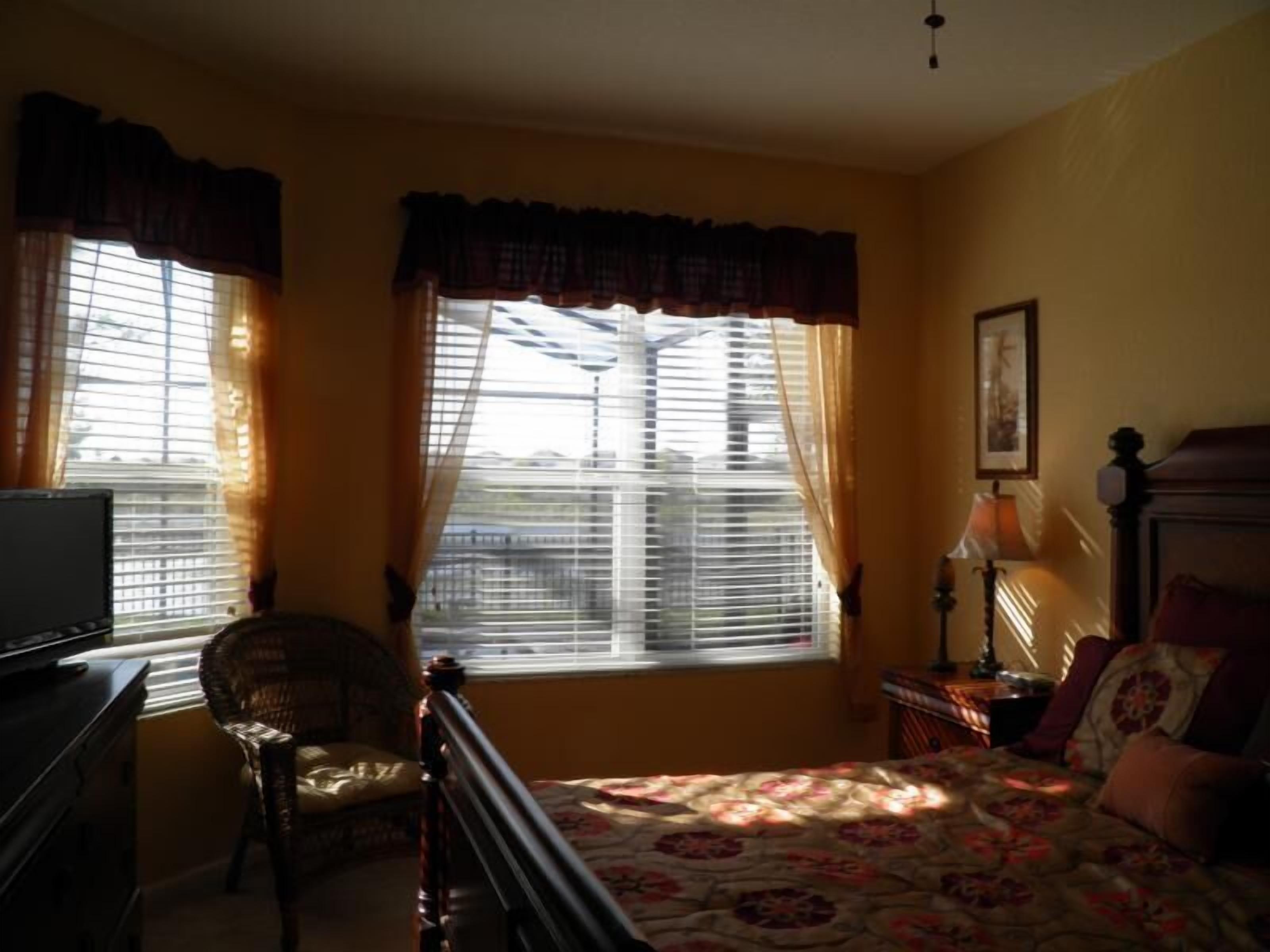 A bedroom with a bed, a chair, a desk, and a window with curtains.