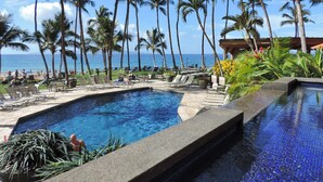 A pool area with lounge chairs and palm trees, overlooking the ocean.