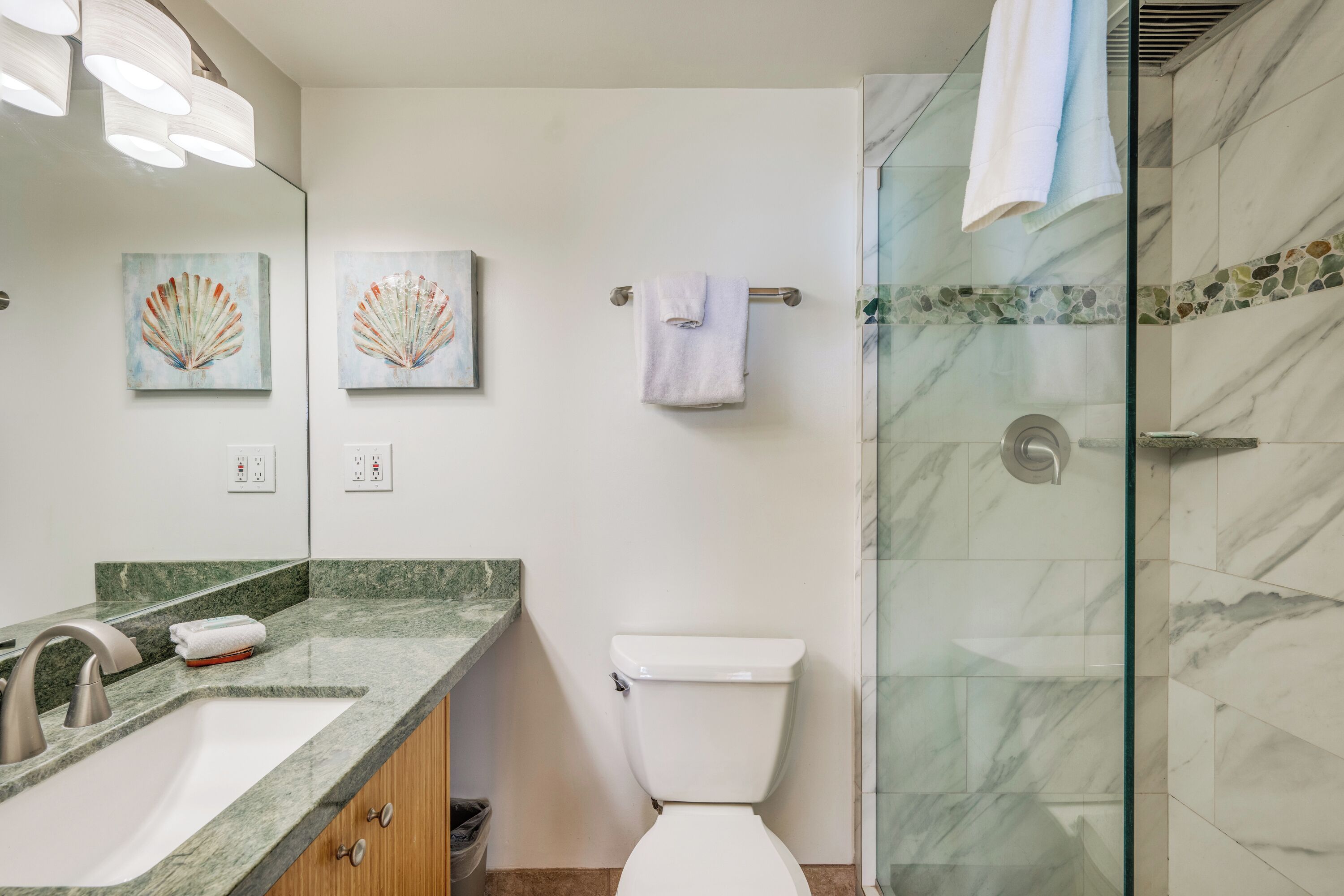 Une salle de bain avec une douche en marbre, des toilettes, un lavabo avec un robinet et deux appliques murales.