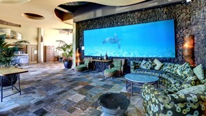 A spacious lobby with a large screen displaying a turtle, stone walls, and a variety of seating arrangements.