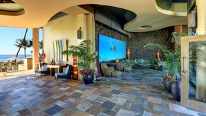 A spacious lounge area with a large screen displaying a turtle, stone flooring, and tropical plants.