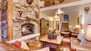 Una sala de estar acogedora con chimenea de piedra, muebles de cuero y una escalera que sube a un nivel superior.