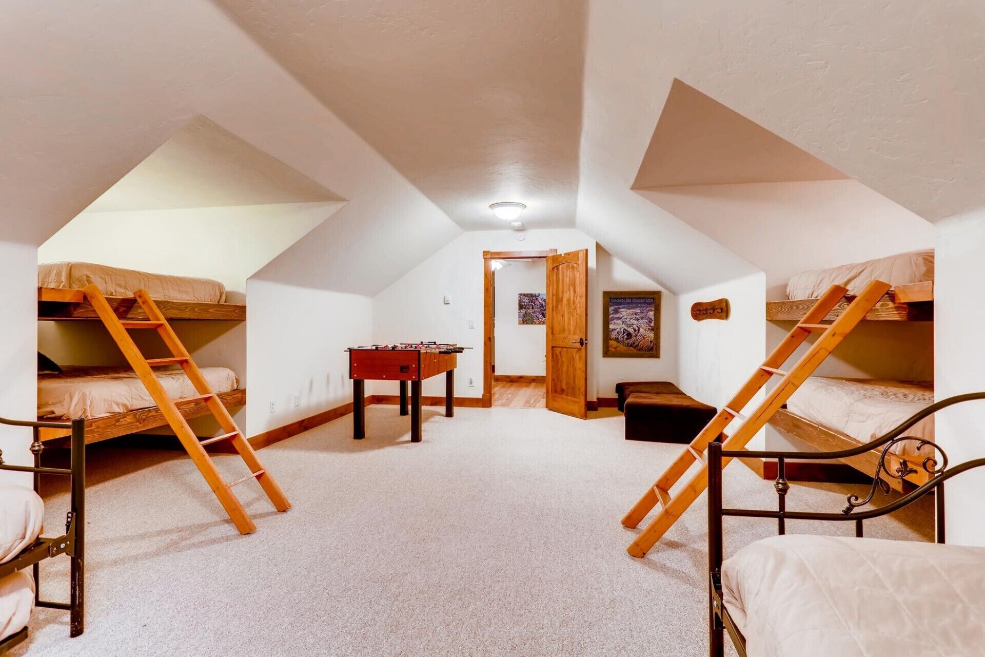Une chambre de dortoir avec des lits superposés, une table de baby-foot et une porte donnant sur une autre pièce.
