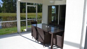 A covered patio with a glass table and wicker chairs, overlooking a grassy area and water. - Beautiful Waterside Villa For Rent In Orlando (Clermont)