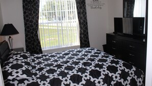 A bedroom with a bed, a dresser, a lamp, and a window with curtains. - Beautiful Waterside Villa For Rent In Orlando (Clermont)