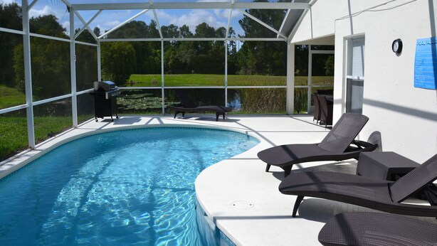 A swimming pool with lounge chairs, a covered patio, and a view of the surrounding landscape. - Beautiful Waterside Villa For Rent In Orlando (Clermont)