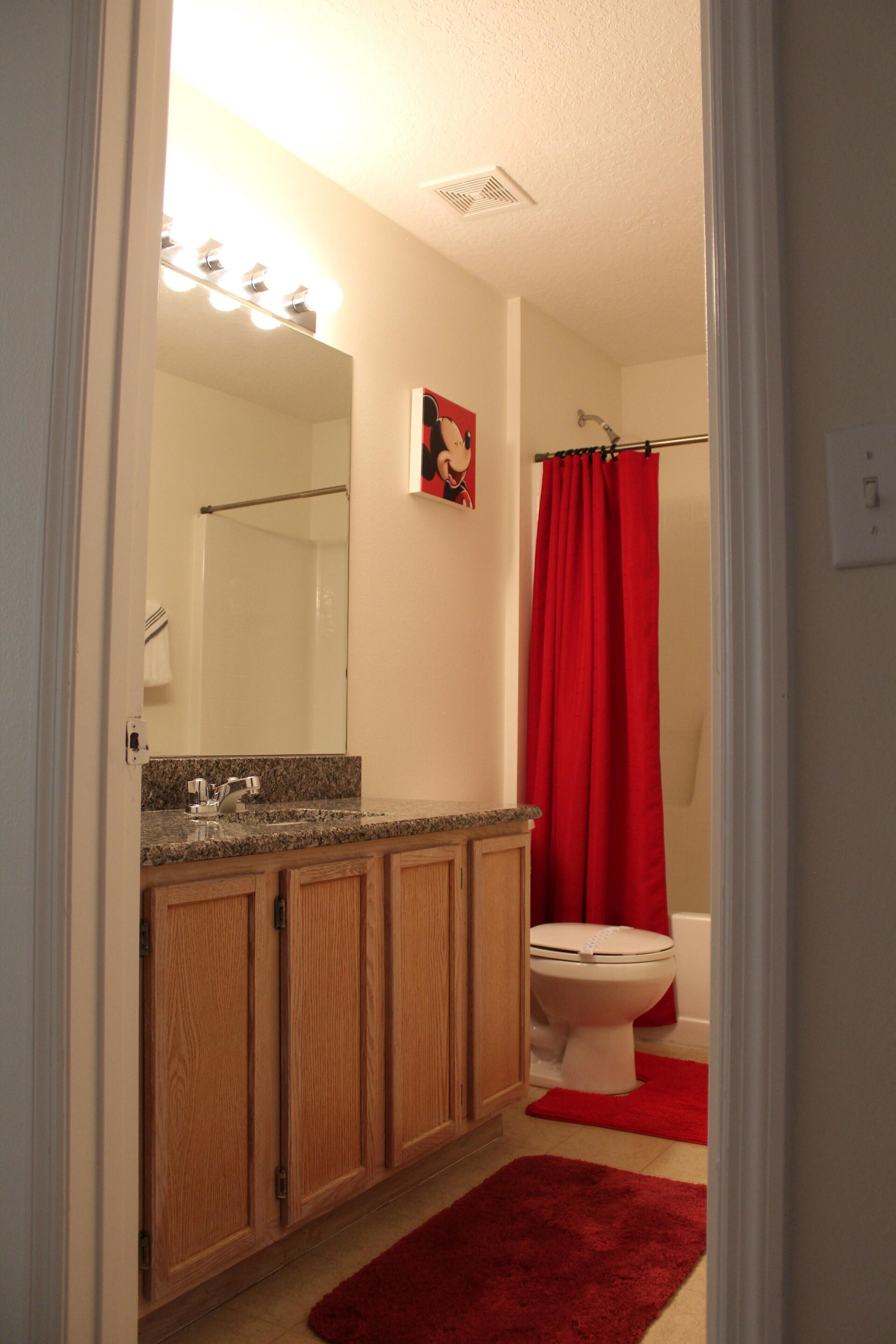 Une salle de bain avec des meubles en bois, un lavabo, un miroir, un rideau de douche rouge et des toilettes.