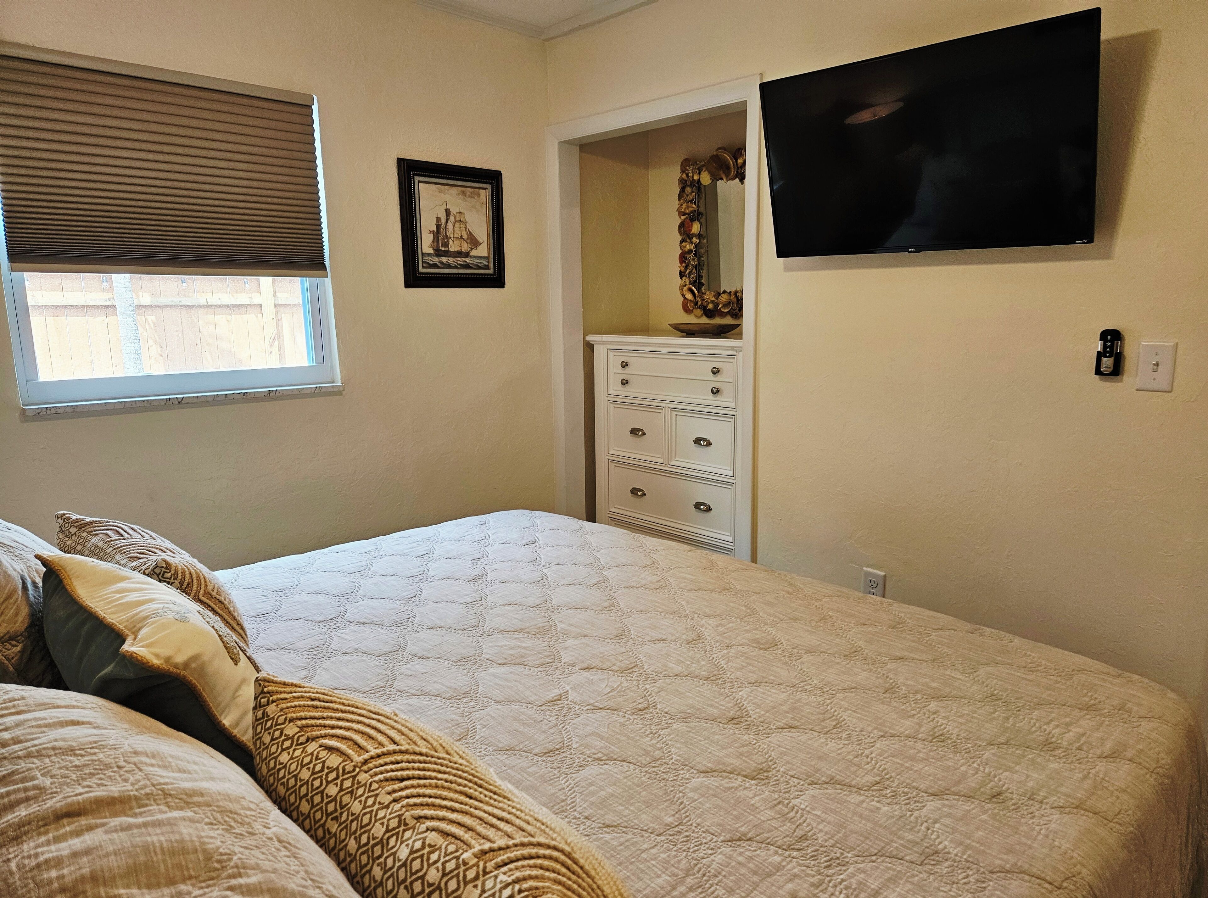 A bedroom with a bed, a dresser, a television, and a window with blinds.