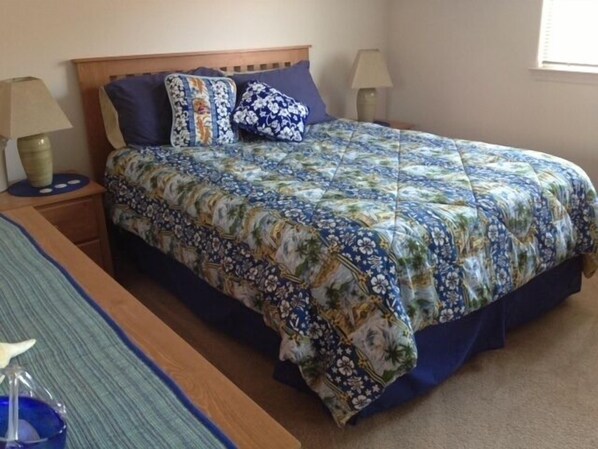 Een netjes opgemaakt bed met een bloemenprint deken en passende kussens, een nachtkastje met een lamp, en een andere nachtkastje met een lamp.