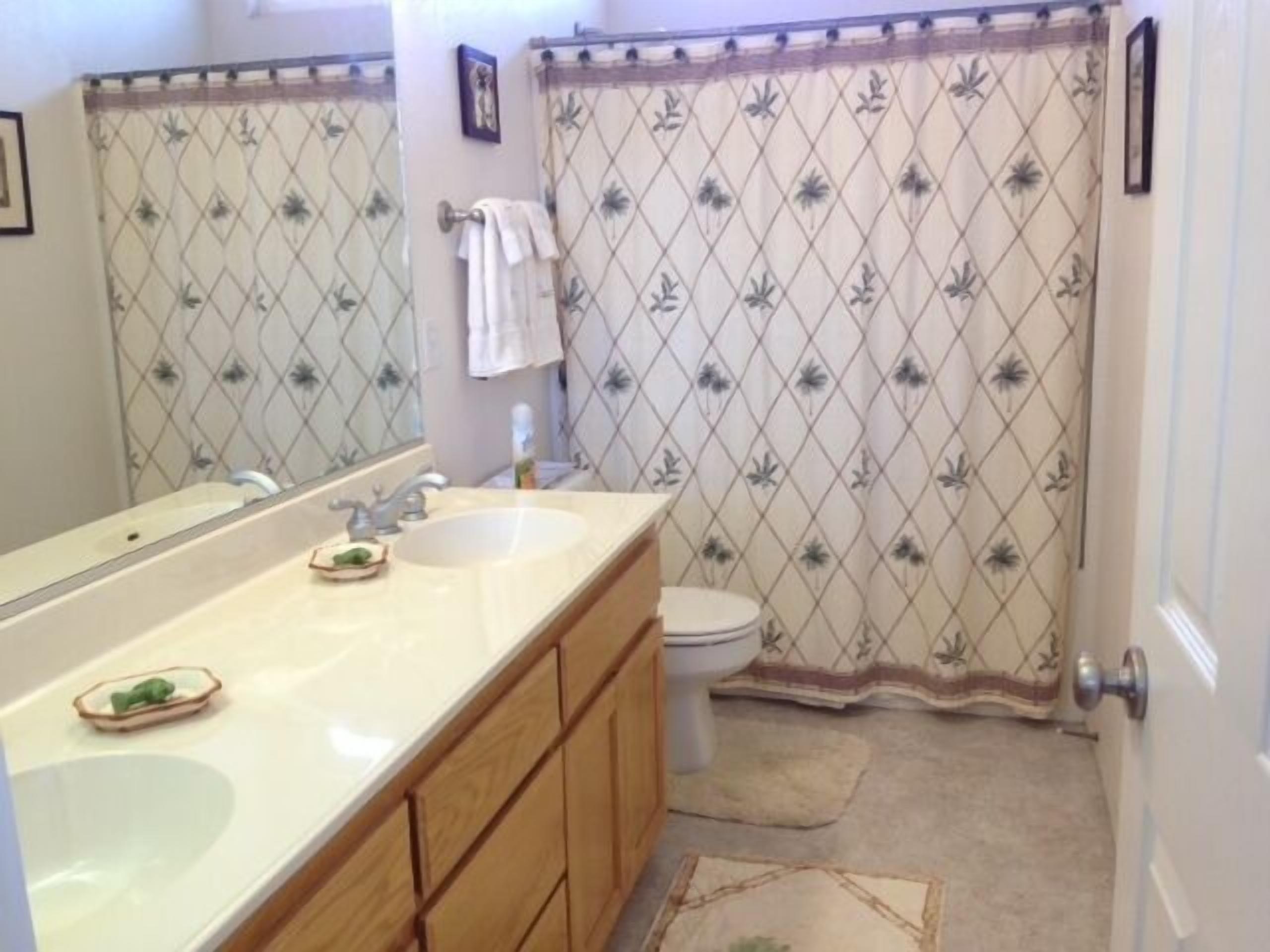 A bathroom with a double sink vanity, a toilet, and a shower curtain with a floral pattern.
