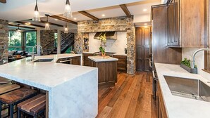 A spacious kitchen with a large island, wooden beams, stone accents, and modern lighting.
