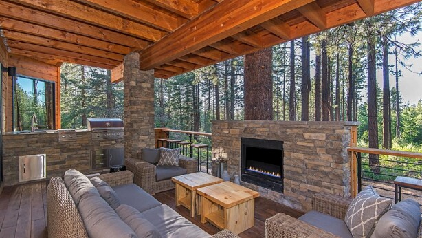 An outdoor living area with a stone fireplace, wicker furniture, and a view of a forest.