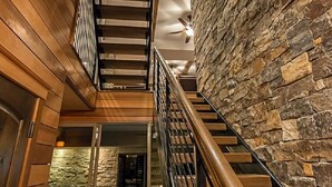A multi-level interior with a wooden staircase, stone walls, and a glass-enclosed pool area.