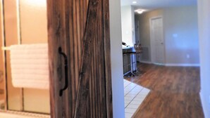 Une pièce dotée d’une porte en bois de style grange, d’un coin cuisine équipé d’appareils modernes et d’un couloir menant à une autre pièce.