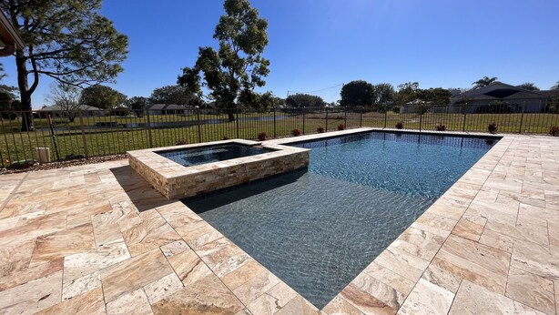 Une piscine rectangulaire bordée de pierres, entourée d’une terrasse dallée.