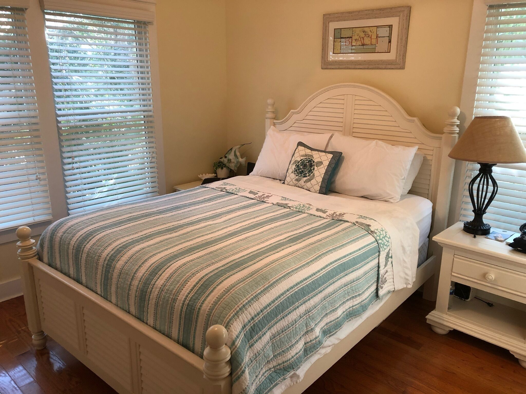 A neatly made bed with striped bedding, a bedside lamp, and a framed picture on the wall.