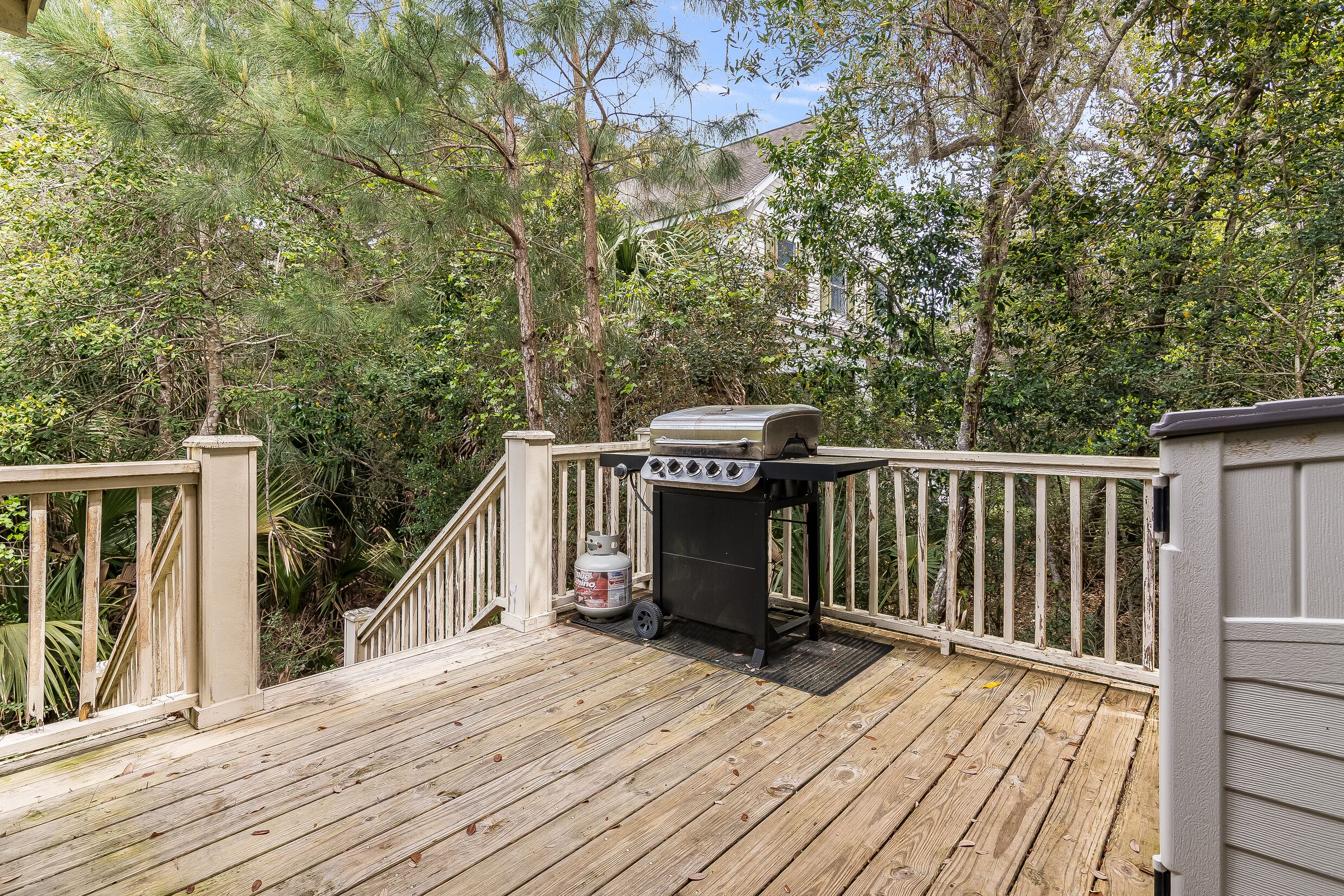 A wooden deck with a barbecue grill and propane tank.