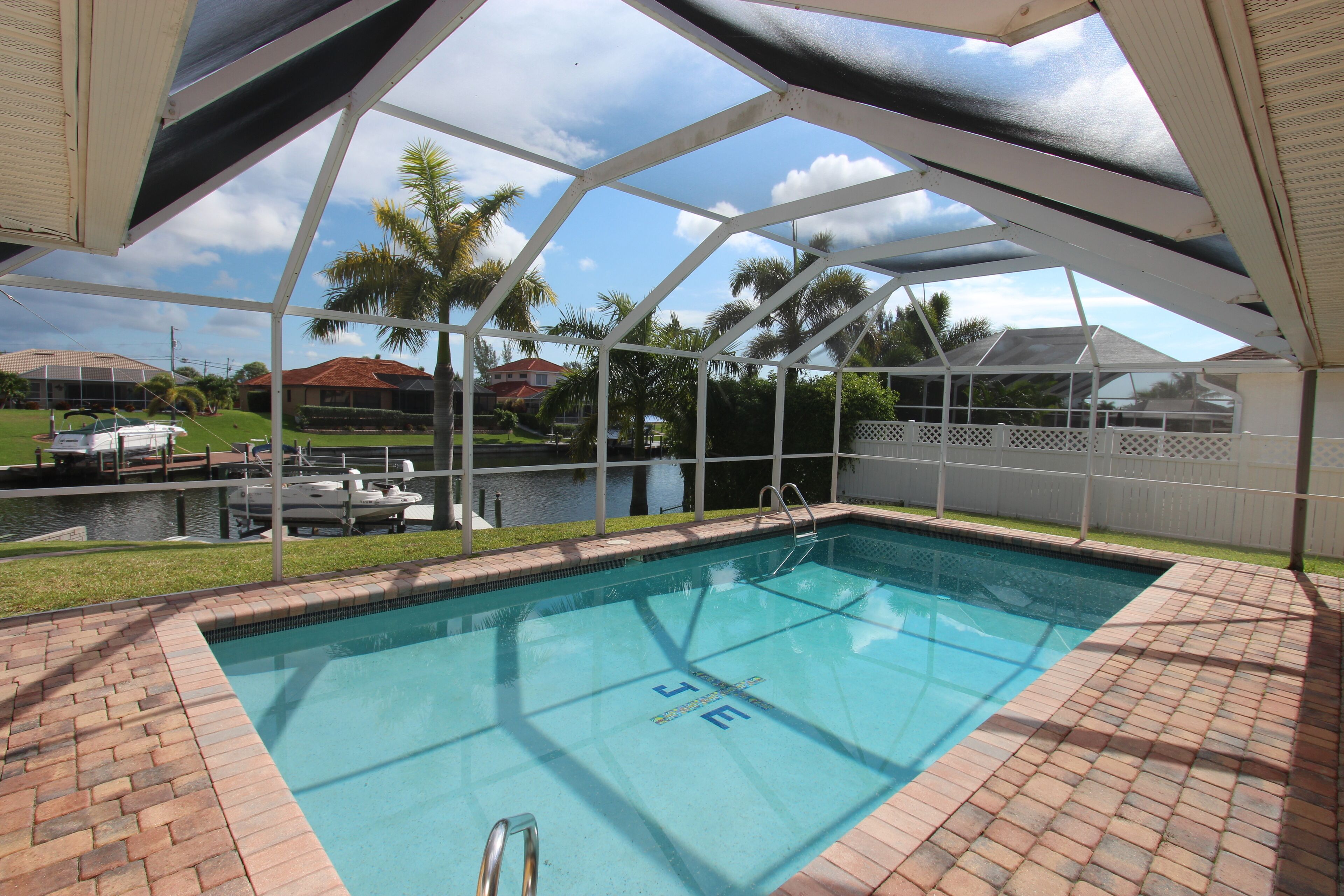 A swimming pool with a clear view of the surrounding area, including a boat dock and a house in the background.