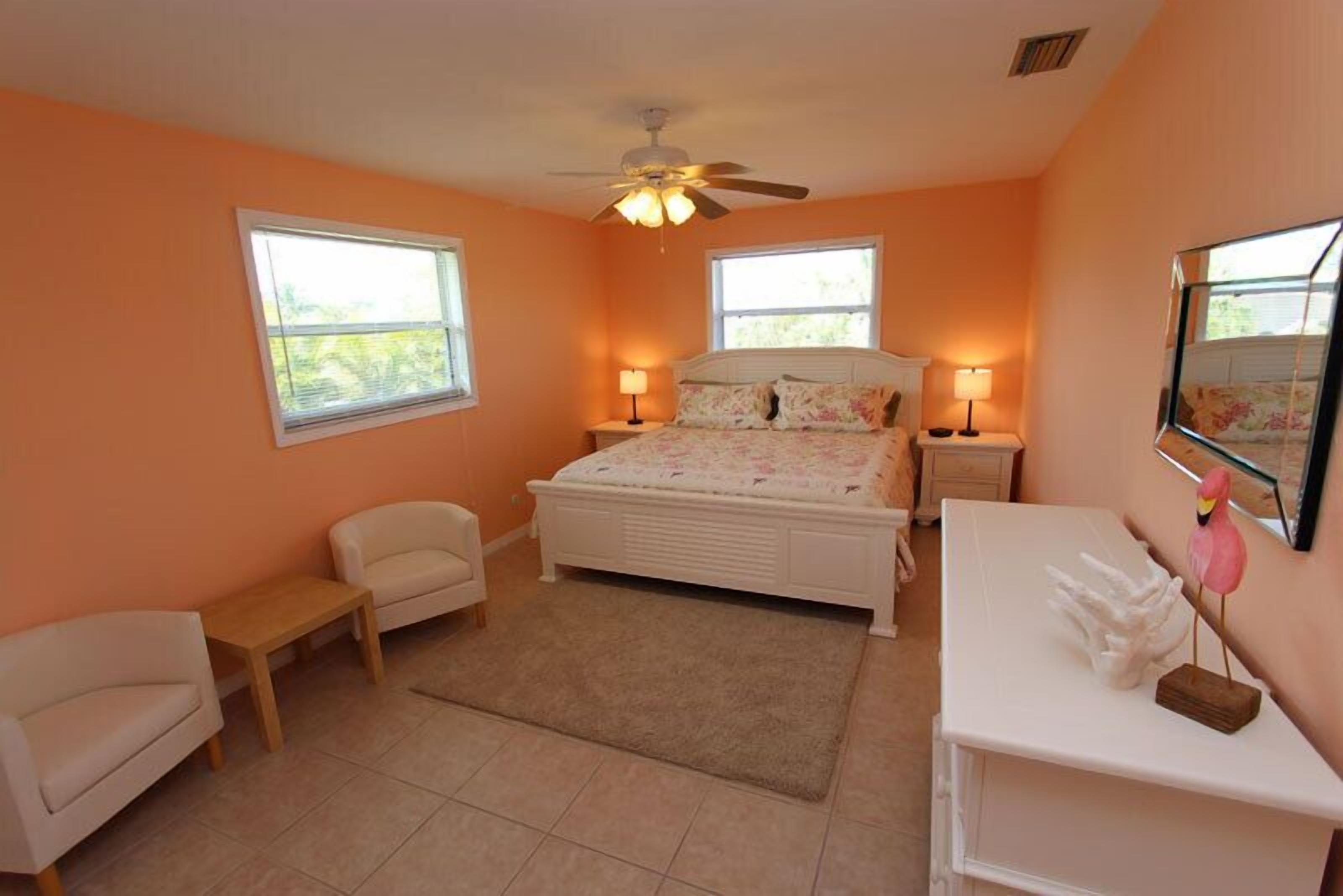 A bedroom with a bed, two bedside tables, a chair, a desk, and a ceiling fan.