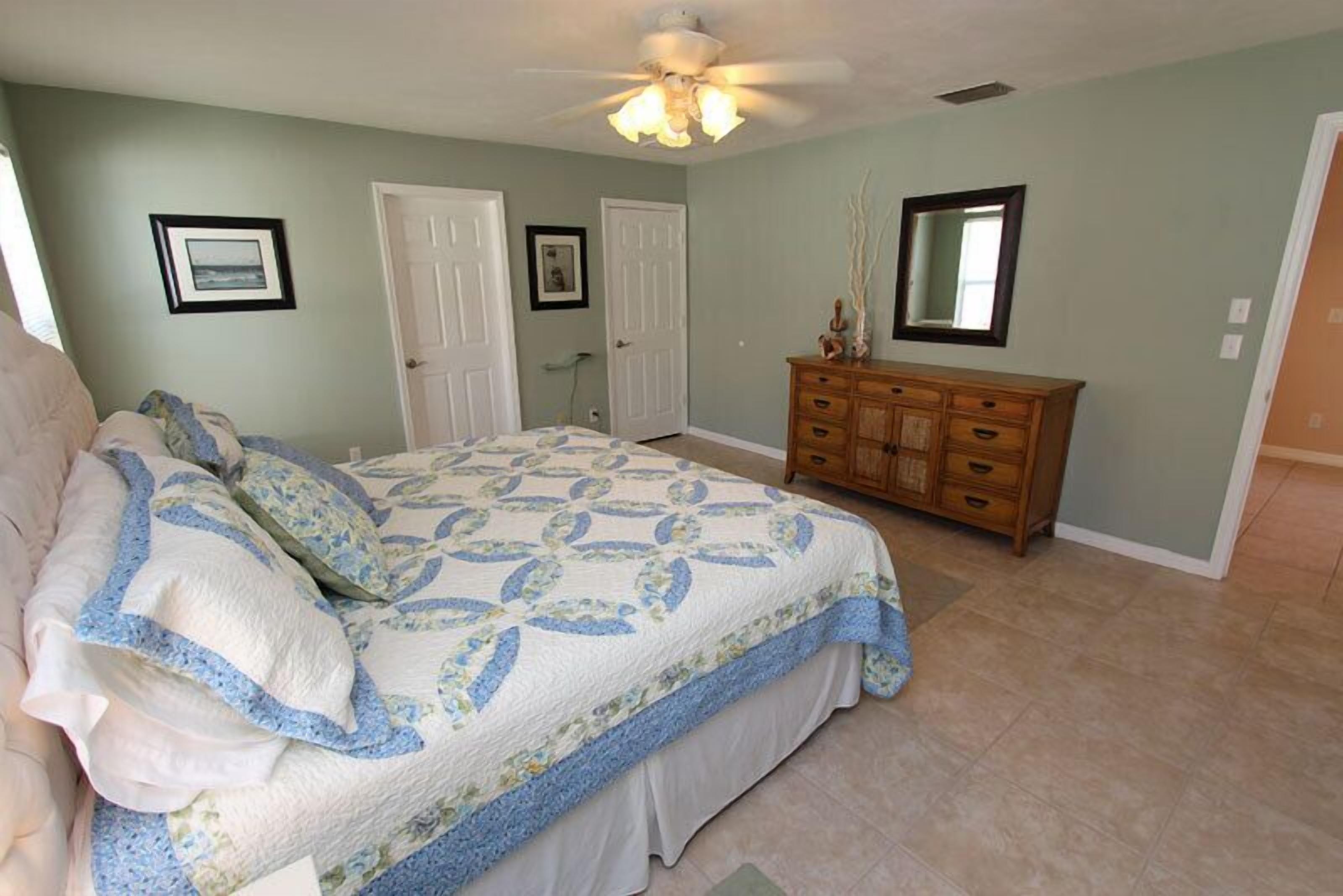 A bedroom with a bed, a dresser, a ceiling fan, and two doors.
