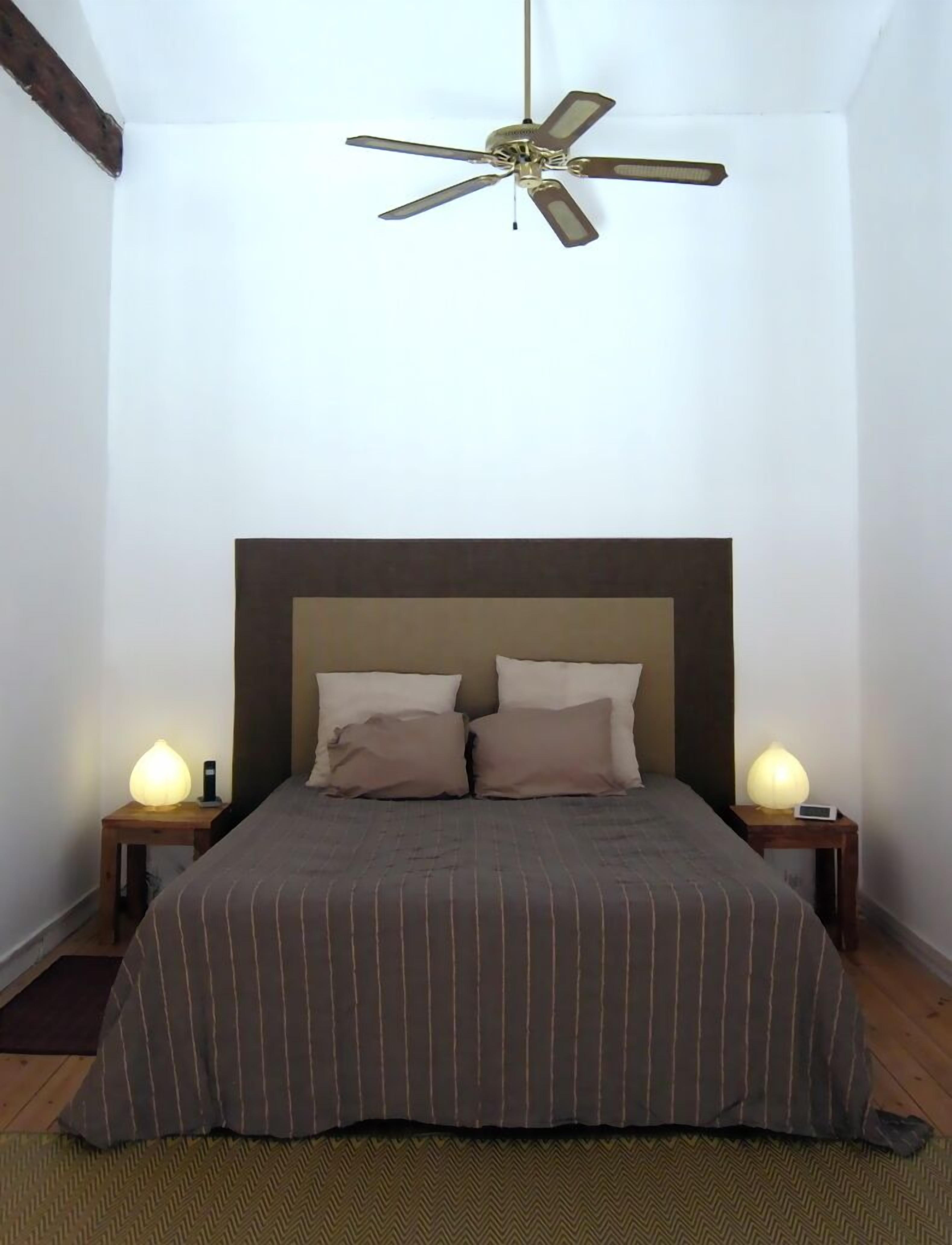 Een slaapkamer met een bed, twee nachtkastjes, een plafondventilator en twee wandlampen.