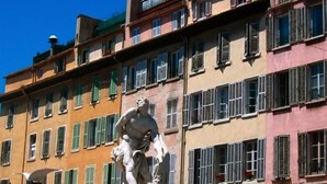 Eine klassische Statue vor einem mehrstöckigen Gebäude mit Balkonen und Fensterläden.