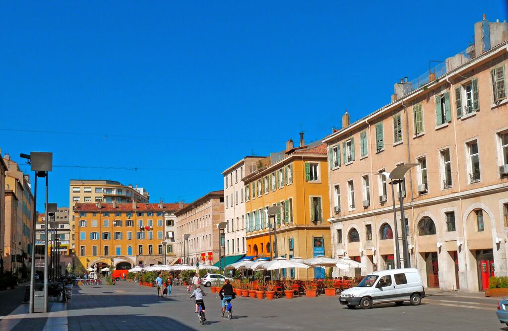 A street with buildings, outdoor seating, and people.