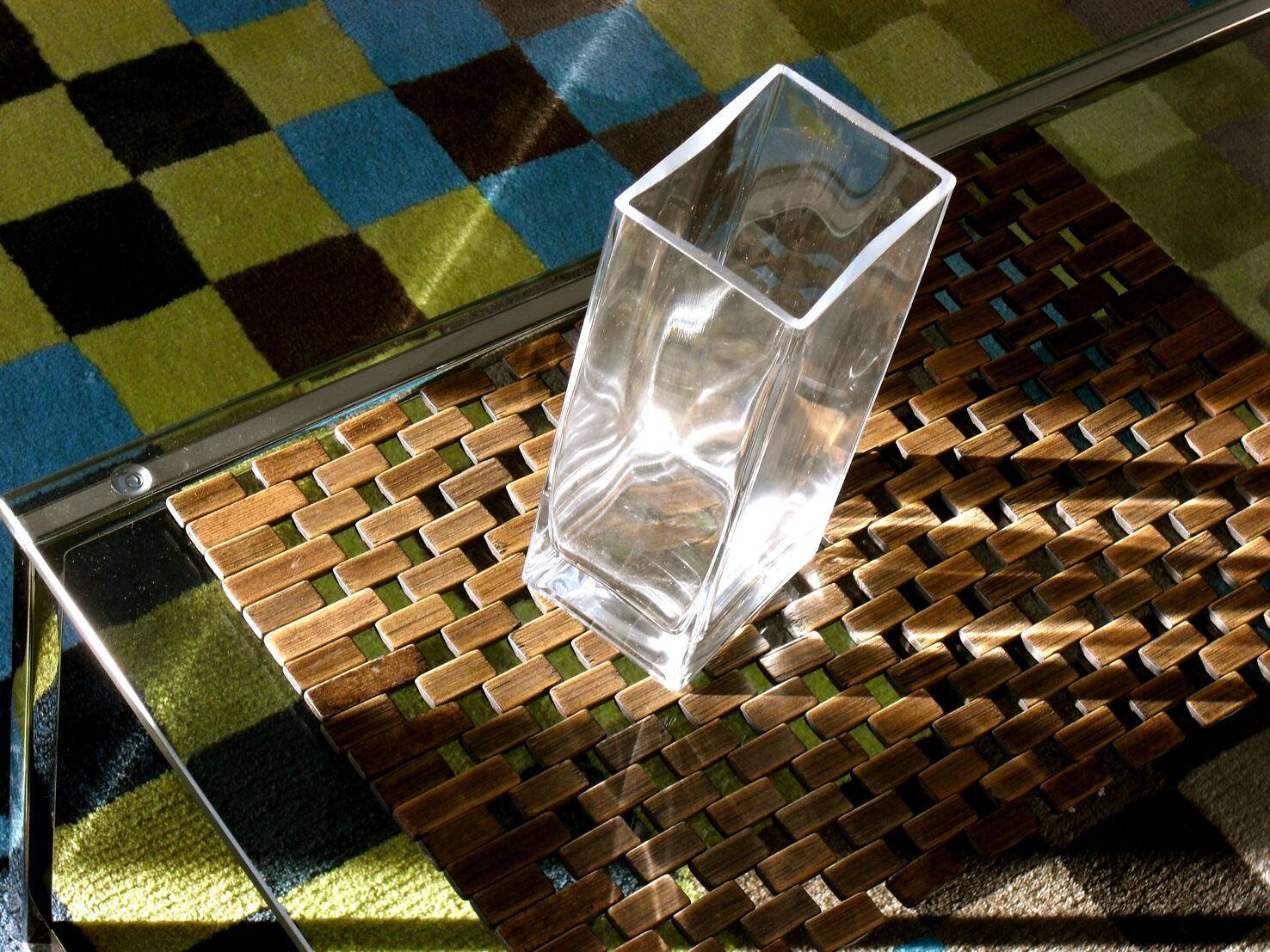 A clear glass vase on a woven metal table.