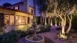 A well-lit house with a fountain in the garden, surrounded by trees and a gravel path. -  MOROCCAN POOL/SPA VILLA IN PALM SPRINGS GREAT DEEPWELL NEIGHBORHOOD
  PS ID106 (Palm Springs)
