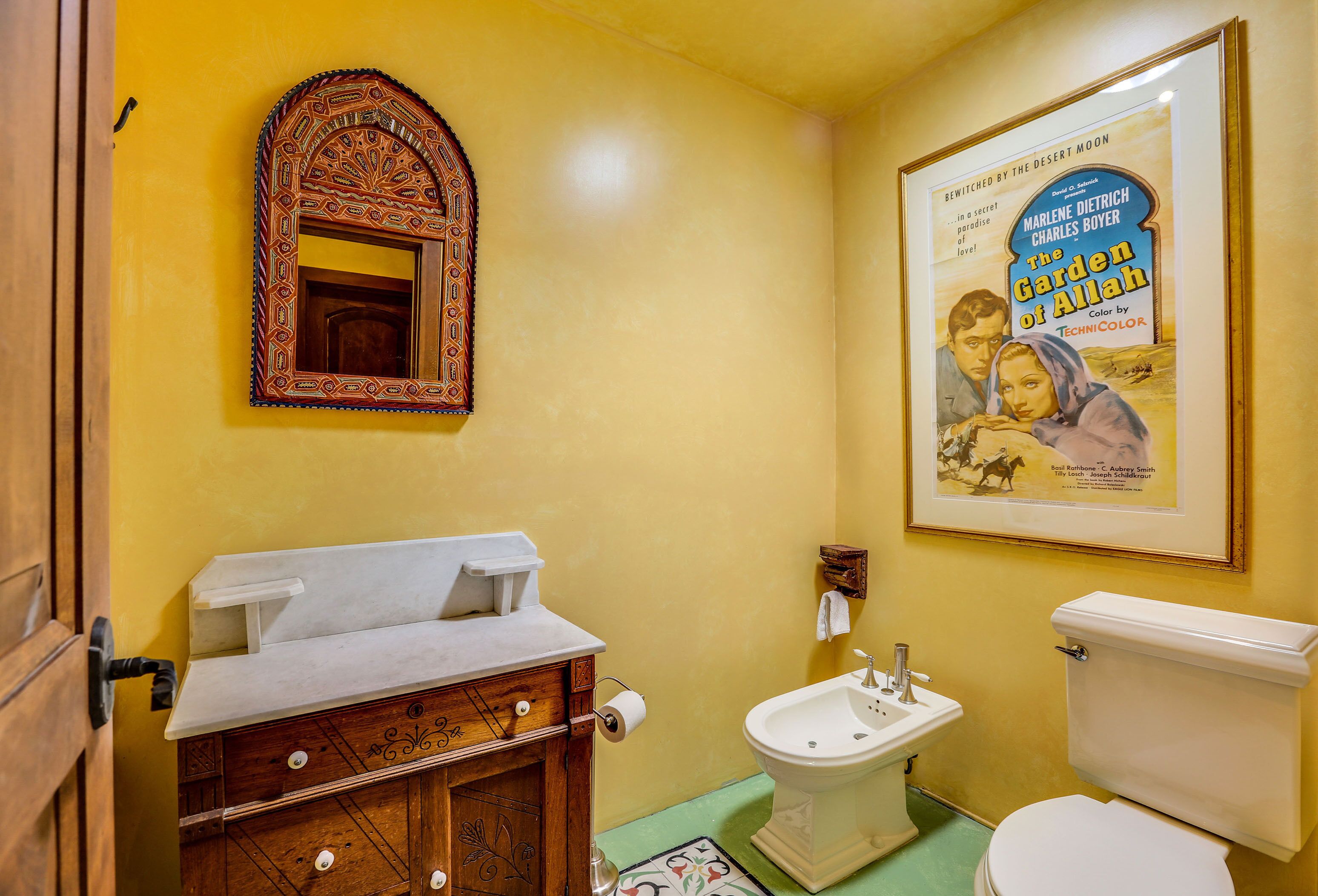 A bathroom with a wooden vanity, a white sink, a pedestal sink, and a toilet. There is a framed movie poster on the wall.