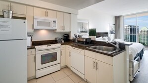 Cocina moderna con armarios blancos, microondas, estufa y lavaplatos. Hay una ventana con vista a la ciudad.