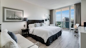 Una habitación de hotel moderna con una cama grande, un escritorio, una silla y vistas a la ciudad.