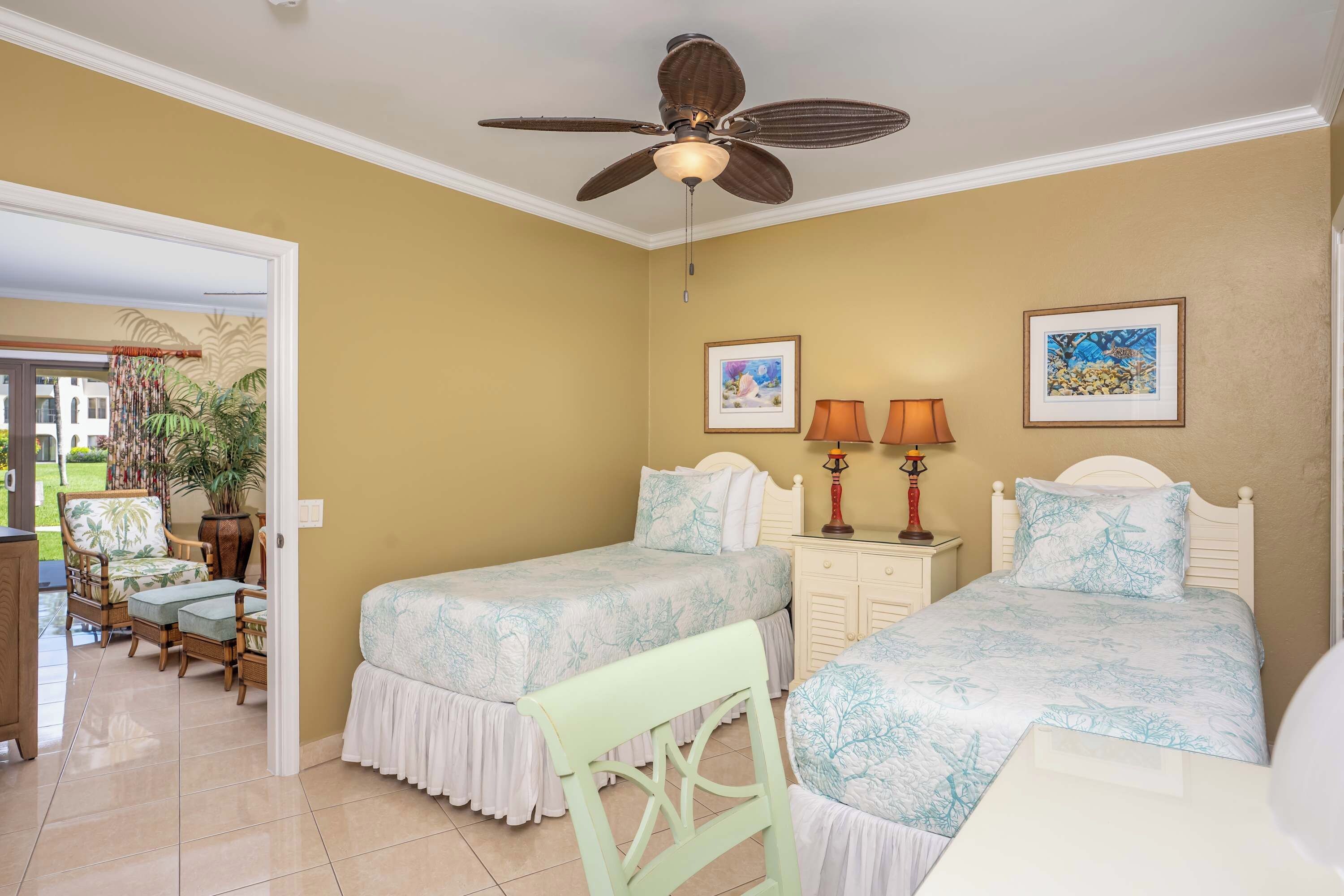 Une chambre d’hôtel avec deux lits, un ventilateur de plafond, un bureau avec une lampe et une chaise.