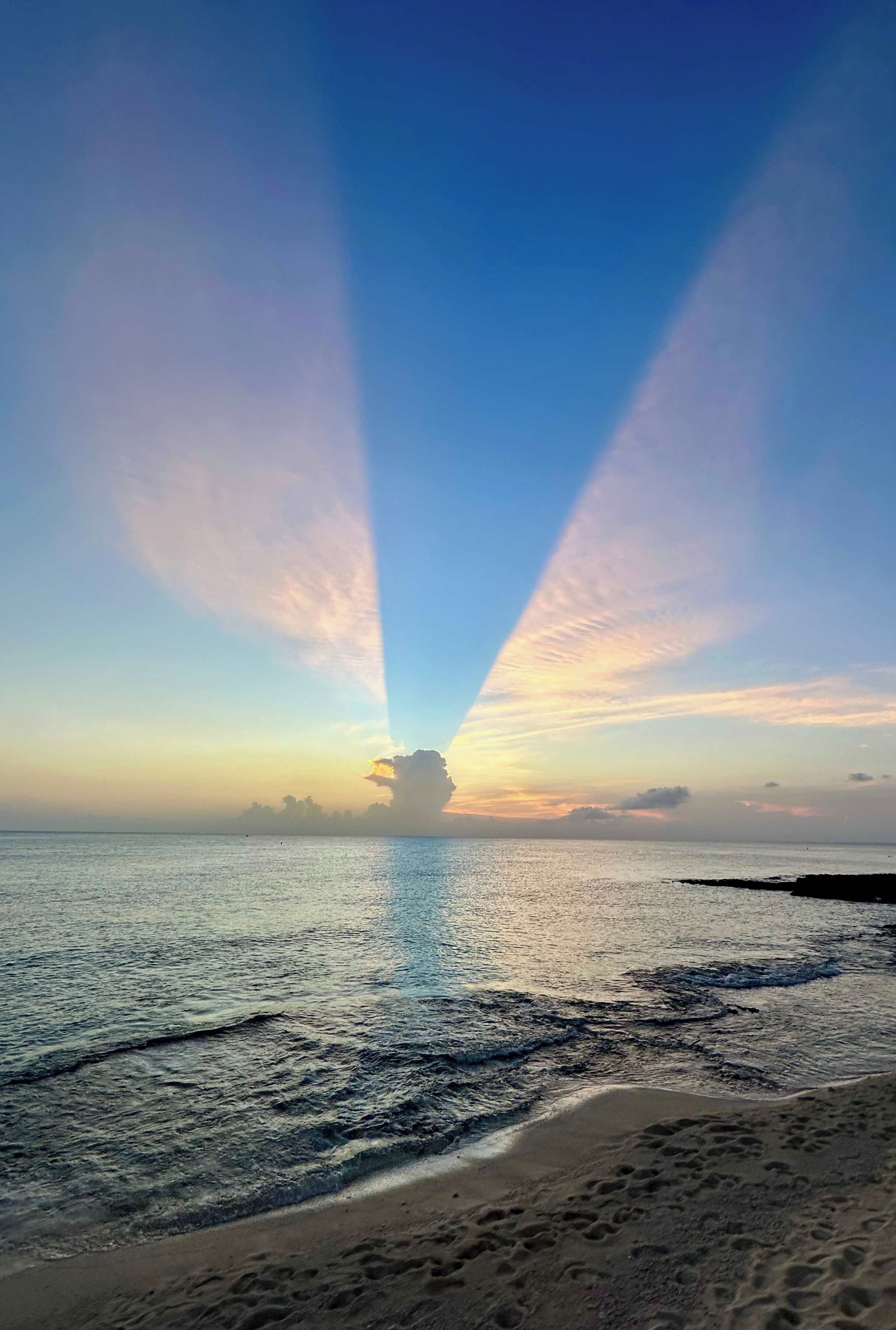 En strand med klart skinnende himmel, roligt hav og et fjerntliggende landskab.